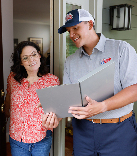 A friendly Robert B. Payne Heating & Air technician in uniform holding a clipboard and discussing service details with a smiling female homeowner at her front door.