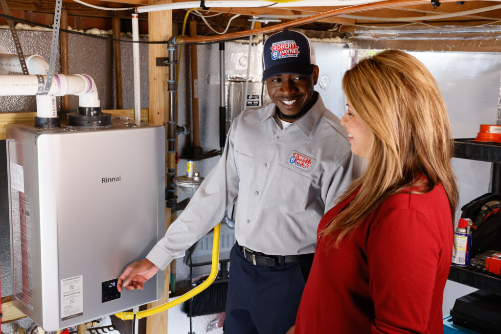 Robert B. Payne technician explains Rinnai tankless water heater to homeowner | Robert B. Payne A smiling Robert B. Payne technician demonstrates the controls of a wall-mounted Rinnai tankless water heater to a woman