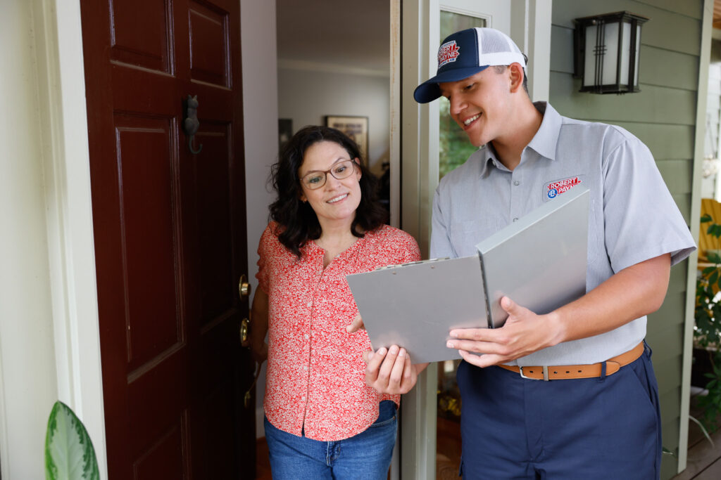 Robert B. Payne technician reviewing paperwork with a customer | Robert B. Payne A smiling Robert B. Payne technician in a branded uniform reviews paperwork on a clipboard with a woman at the entrance of her home